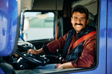 Happy professional truck driver driving his truck and looking at camera.