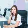 Young woman administrative manager talking on phone sitting behind the reception desk.